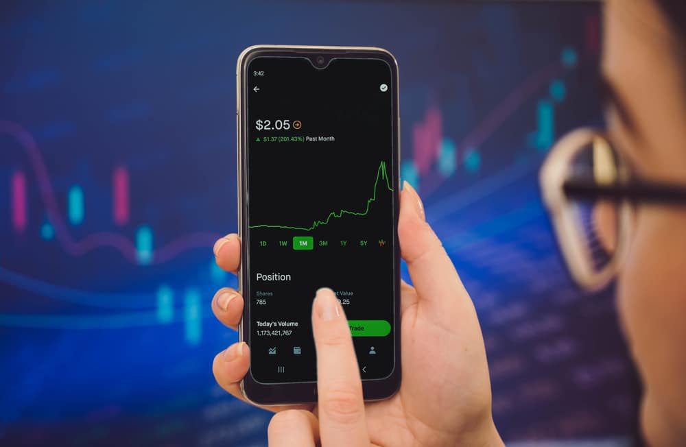 Person holding a smartphone displaying a stock trading app with a rising green chart on the screen